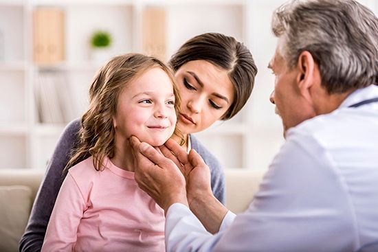 A little girl is being examined by a doctor while her mother looks on.