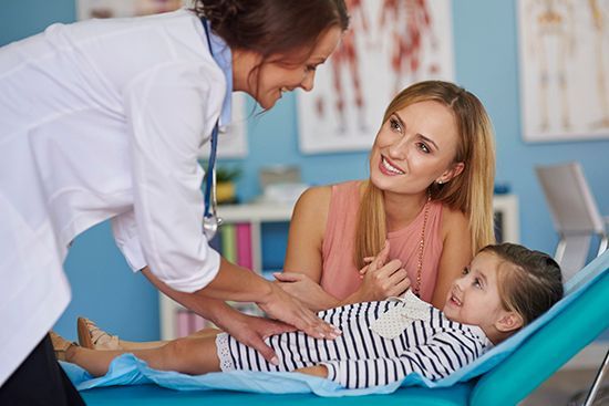 A little girl is laying on a bed talking to a doctor.