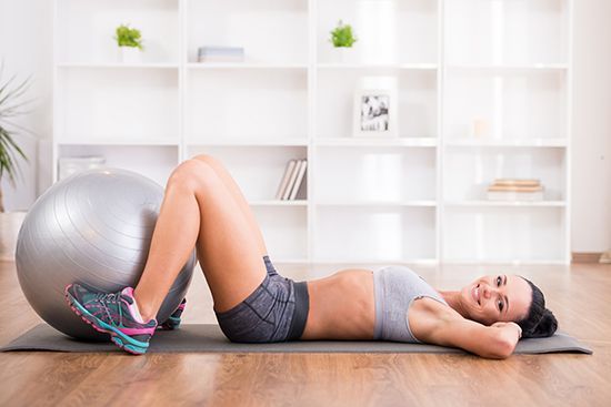 A woman is laying on a yoga mat next to an exercise ball.