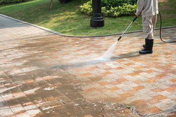 Person power washing a brick walkway with water, near grass and a lamppost.