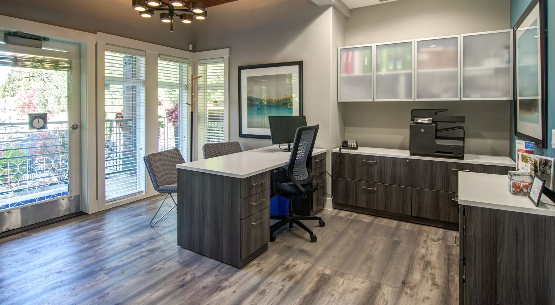 Office space with desk, chair, printer, cabinets, and balcony door at Sofi at Forest Heights, offers apartments for rent in Portland, OR. Gray and white color scheme.