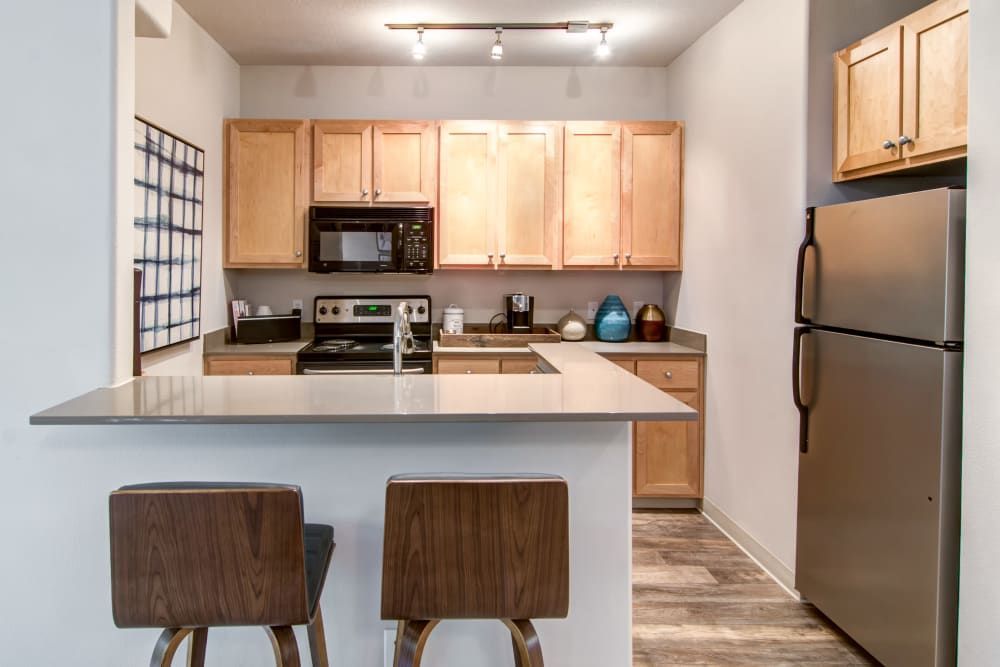 Modern kitchen with light wood cabinets, stainless steel appliances, and a breakfast bar with two stools at Sofi at Forest Heights, offers apartments for rent in Portland, OR.