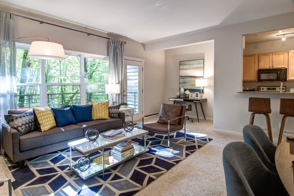 Living room with gray sofa, patterned rug, and access to a balcony with forest view at Sofi at Forest Heights, offers apartments for rent in Portland, OR.