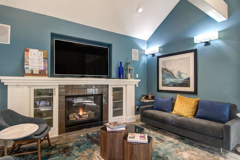 Clubhouse with fireplace, TV, and blue walls; sofa with pillows, wood tables, and armchair at Sofi at Forest Heights, offers apartments for rent in Portland, OR.
