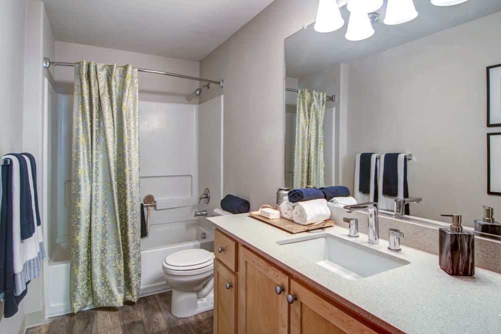 Bathroom with a white tub, toilet, and sink at Sofi at Forest Heights, offers apartments for rent in Portland, OR. Wooden cabinets, gray walls, and a floral shower curtain.