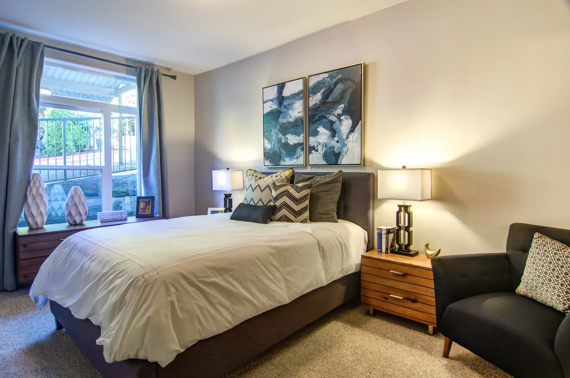 Bedroom with bed, nightstands, armchair, window with curtains, and artwork at Sofi at Forest Heights, offers apartments for rent in Portland, OR.