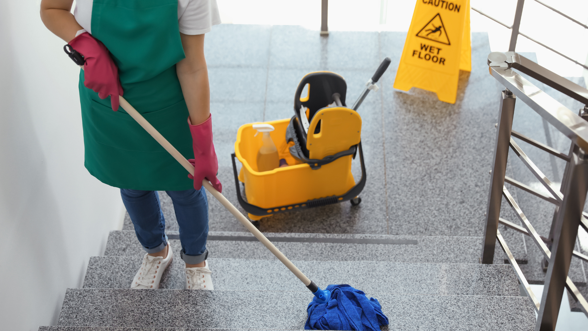 Person mopping stairs with yellow caution sign and cleaning cart nearby