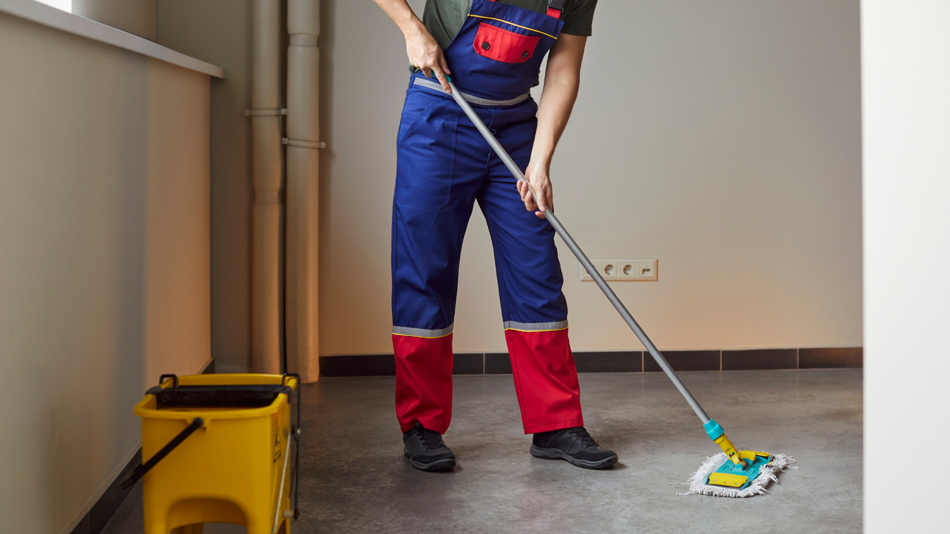 Janitor mopping a floor beside a yellow cleaning bucket in a hallway