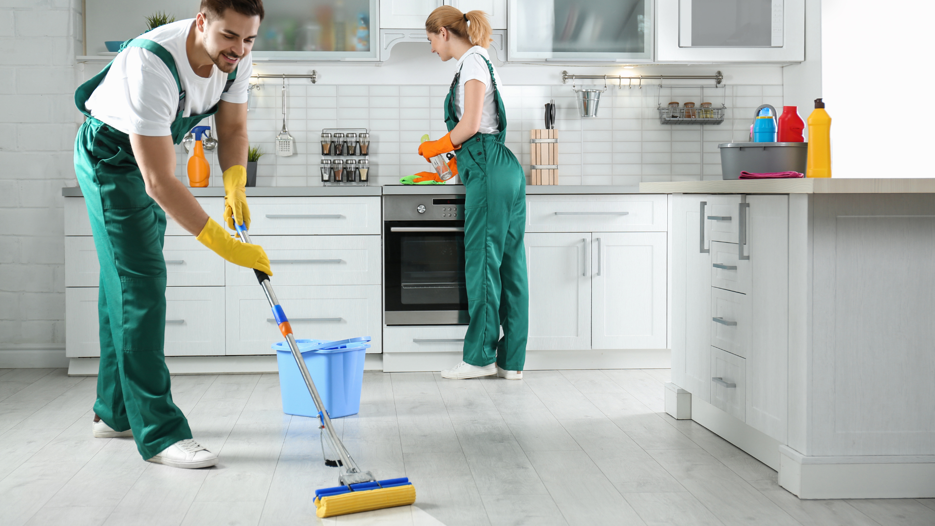 Two cleaners mopping a bright kitchen floor, one in foreground with a blue bucket and yellow mop.