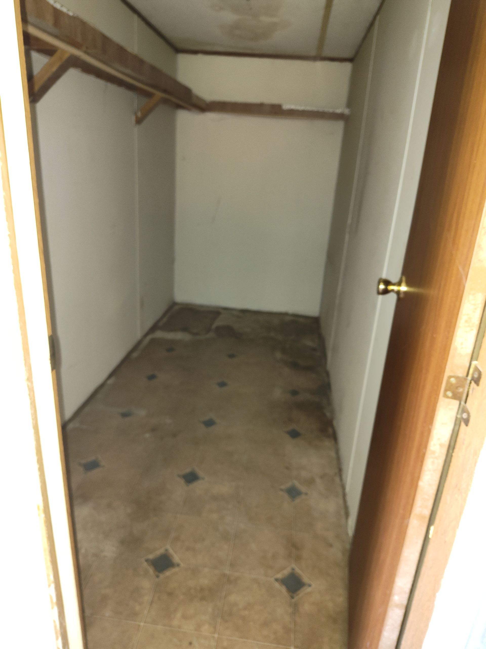 An empty closet with a wooden door and a tiled floor.