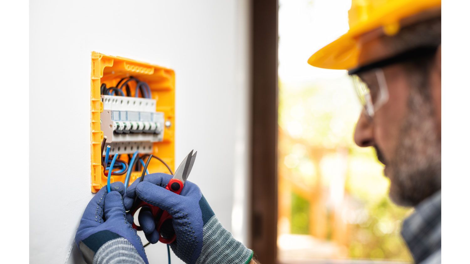 An electrician is working on an electrical box on a wall.