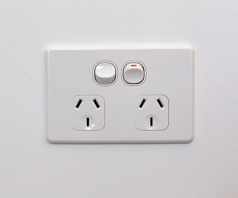 A white electrical outlet with two outlets and a switch on a white wall.