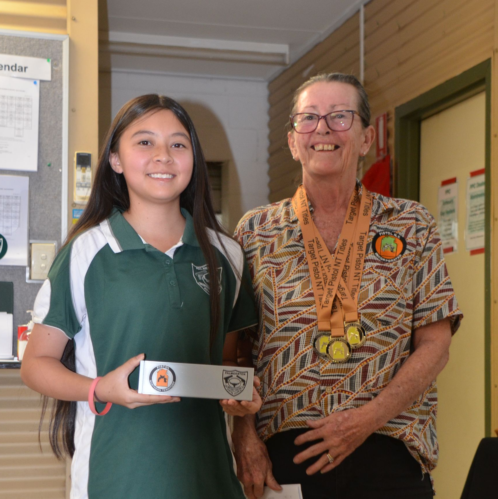 Girl in school uniform and older woman with medals, holding trophy and smiling.