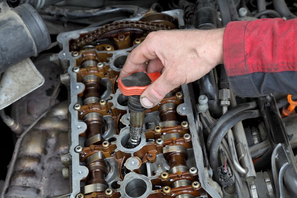 Mecánico utilizando una llave inglesa para ajustar las válvulas del motor dentro del compartimento del motor de un automóvil abierto.