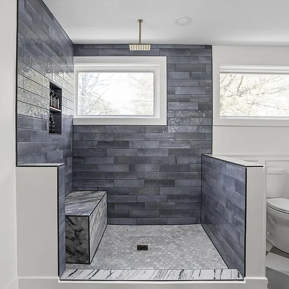Modern tiled walk-in shower with bench and rain showerhead – bathroom remodeling contractor work.