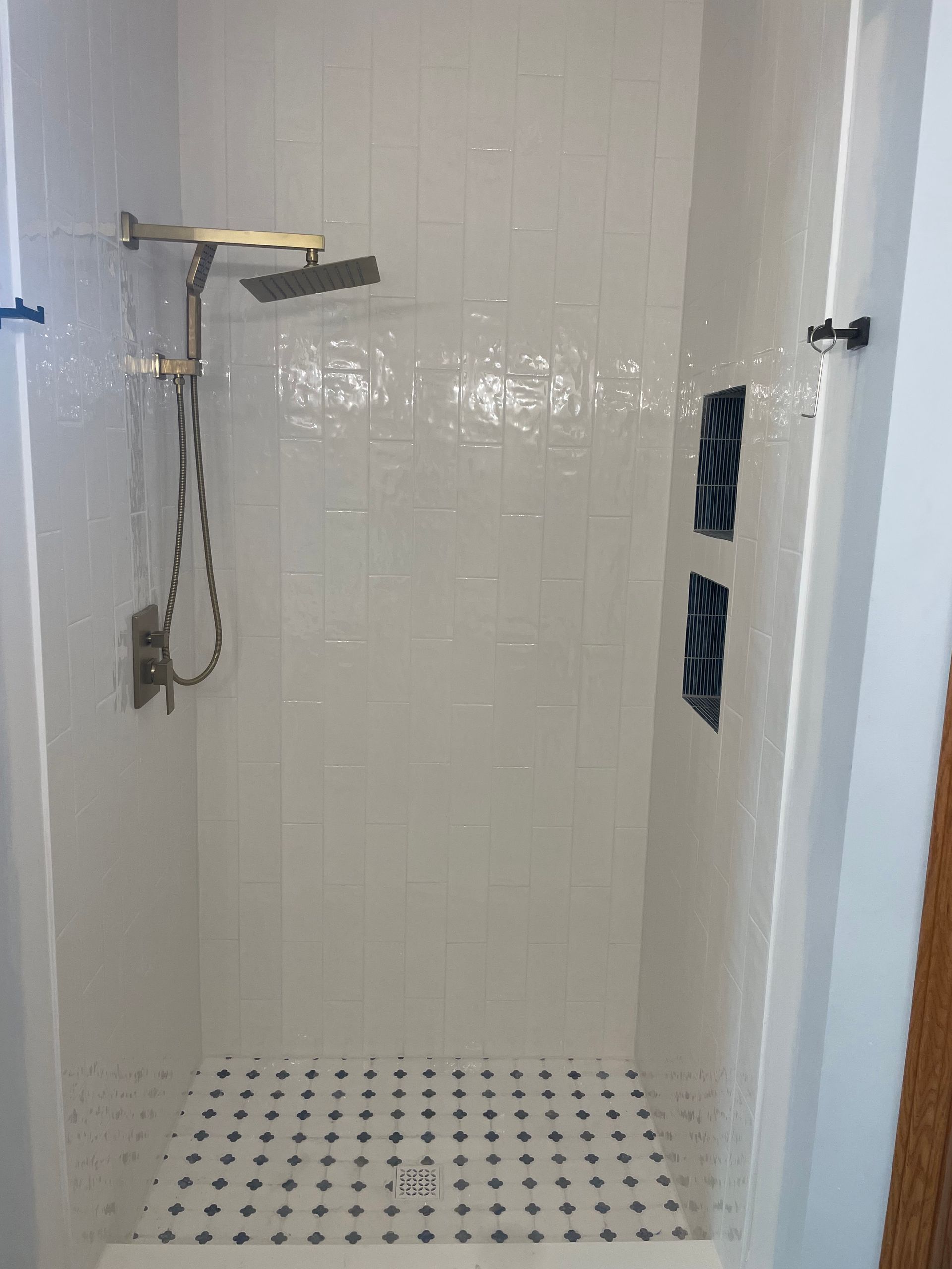 White tiled walk-in shower with brass rain head and blue niche – professional bathroom remodeling contractor service.