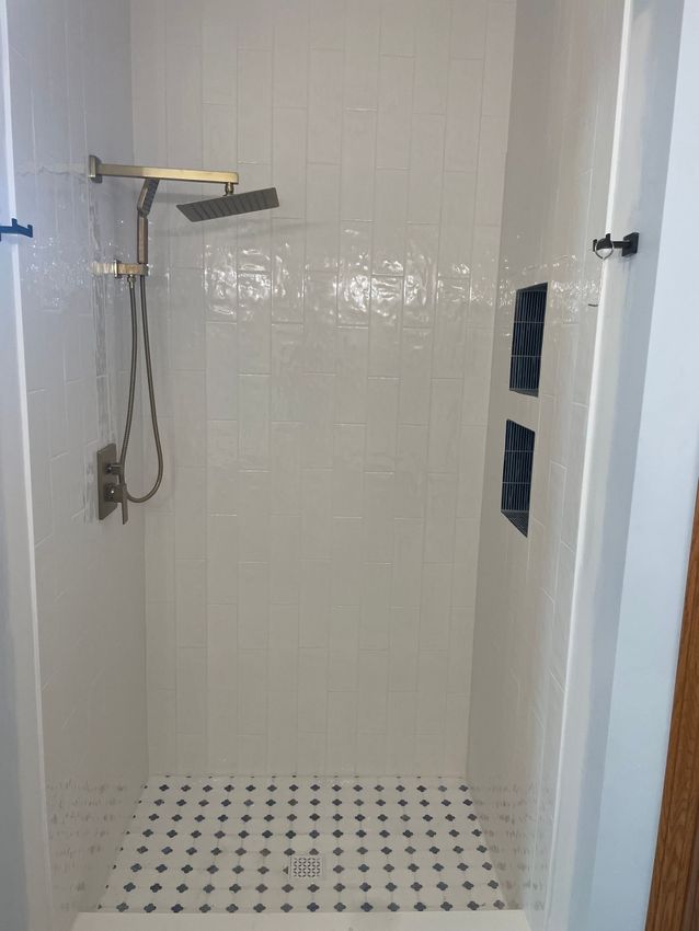 White tiled walk-in shower with brass rain head and blue niche – professional bathroom remodeling contractor service.