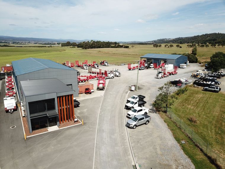 Aerial view of a vehicle depot, showcasing trucks and other machinery, with a large building and surrounding landscape.