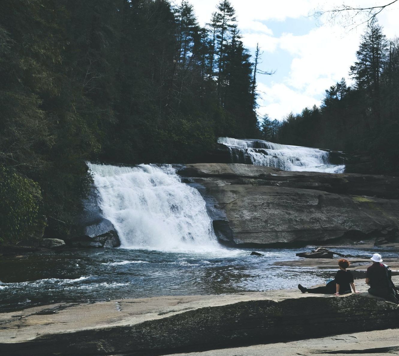 A person sits on a rock near a waterfall