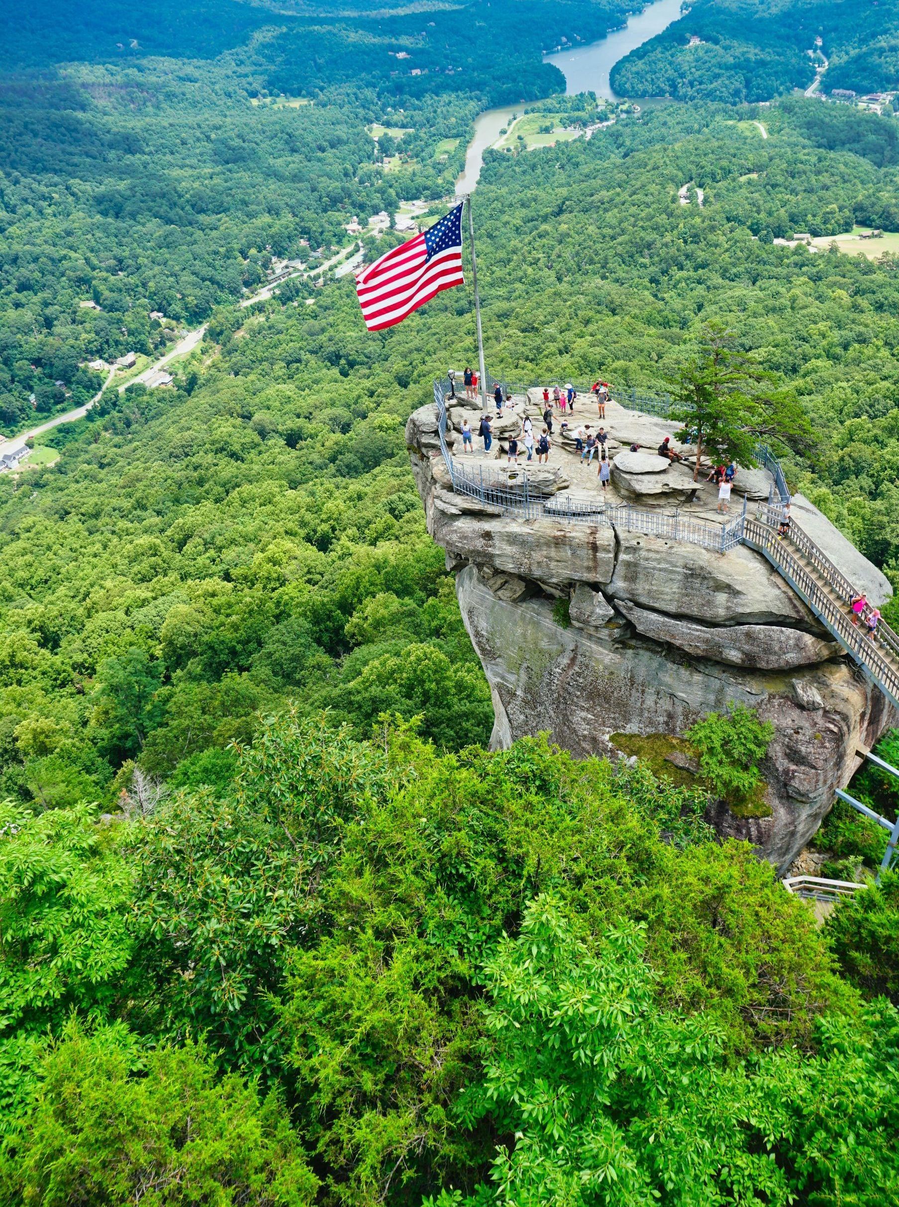 An american flag is flying on top of a rocky cliff surrounded by trees.
