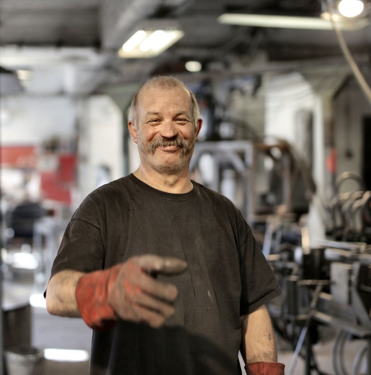 A man wearing a black shirt and red gloves smiles for the camera