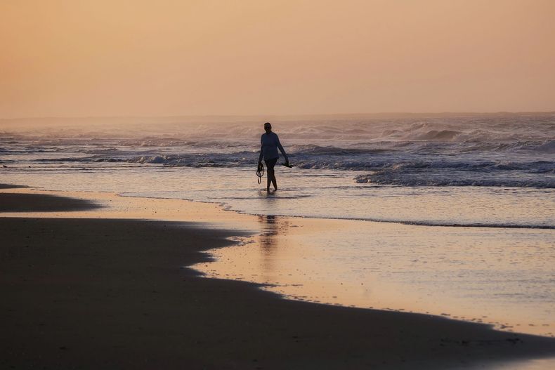 A person is walking on the beach at sunset