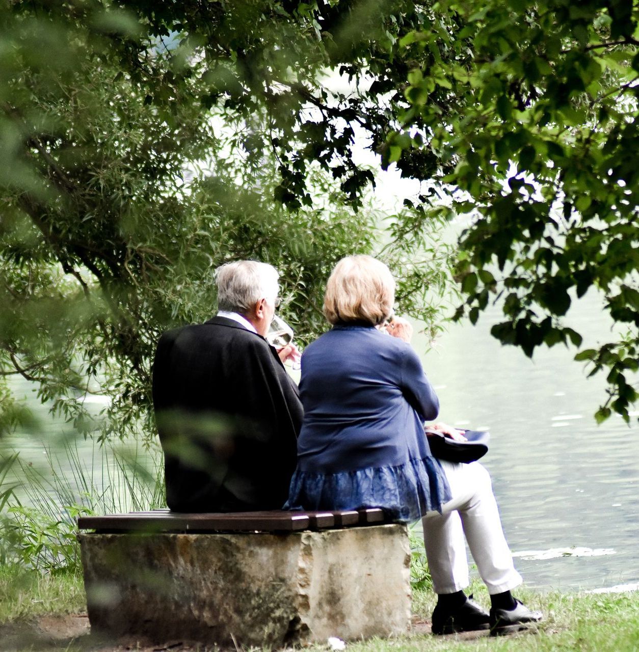 A man and a woman sit on a bench near a body of water