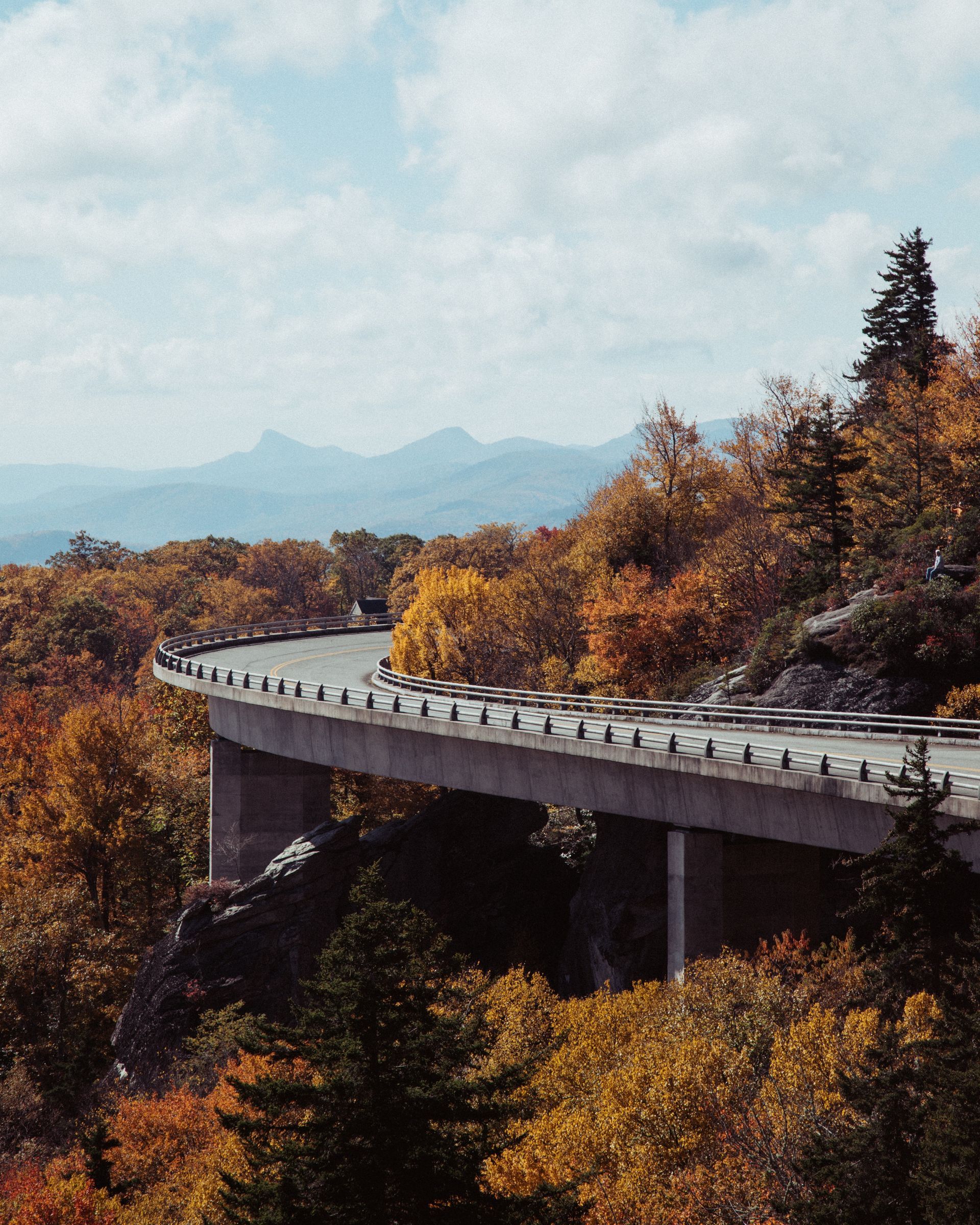 A bridge over a road surrounded by trees with mountains in the background