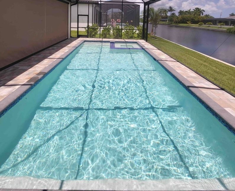 Long narrow backyard pool with clear blue water beside a lawn and screened patio.