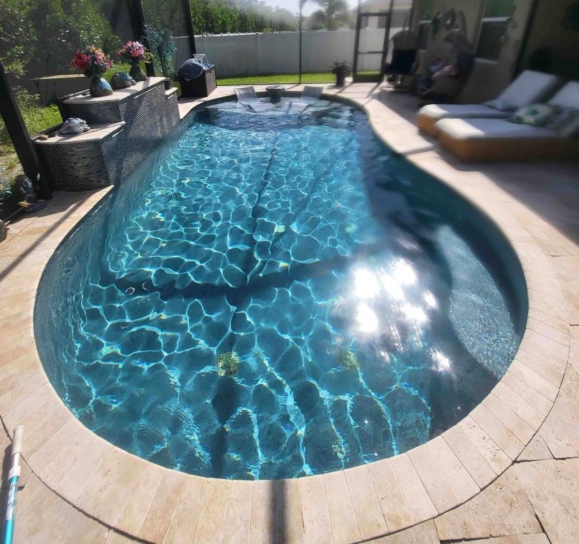 Backyard swimming pool with bright blue water, stone deck, and lounge chairs in sunlight