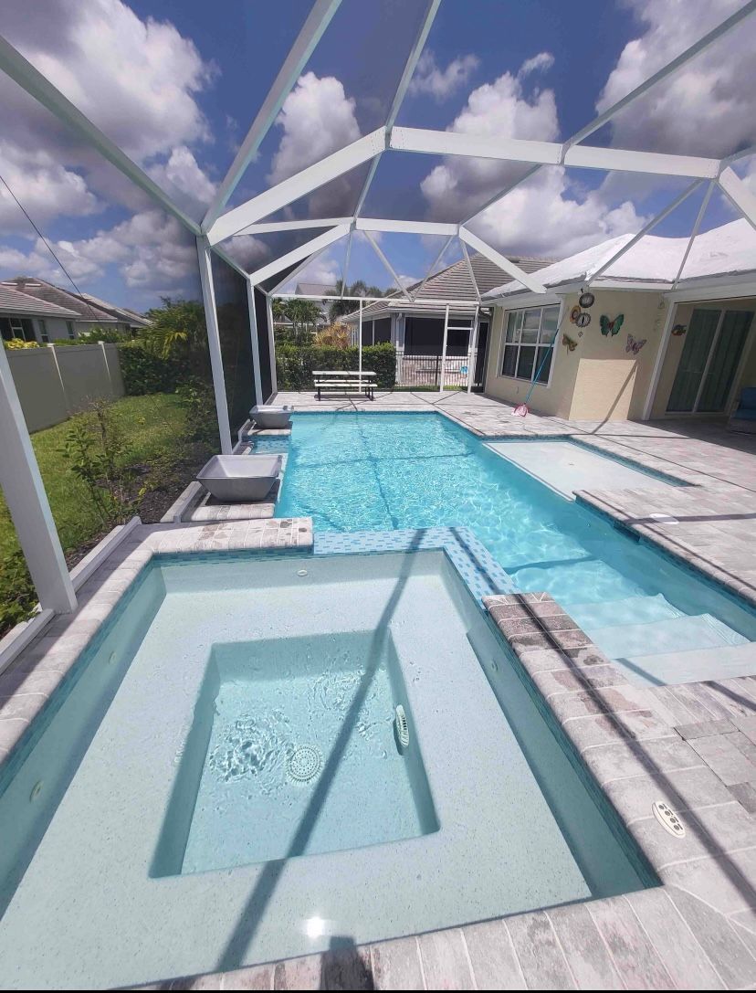 Backyard pool with a spa, white patio, and screened enclosure under a partly cloudy sky