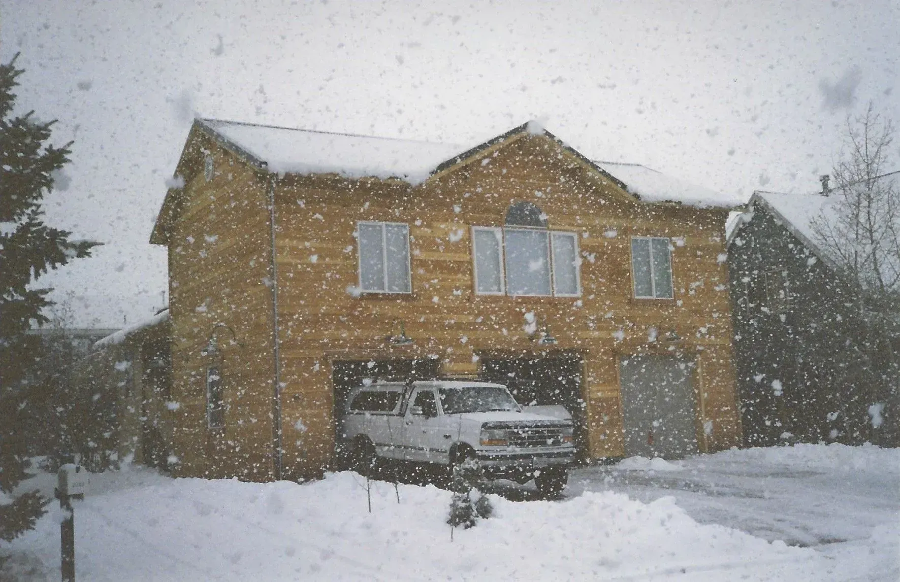 Snow-covered suburban house with a car in the driveway during heavy snowfall