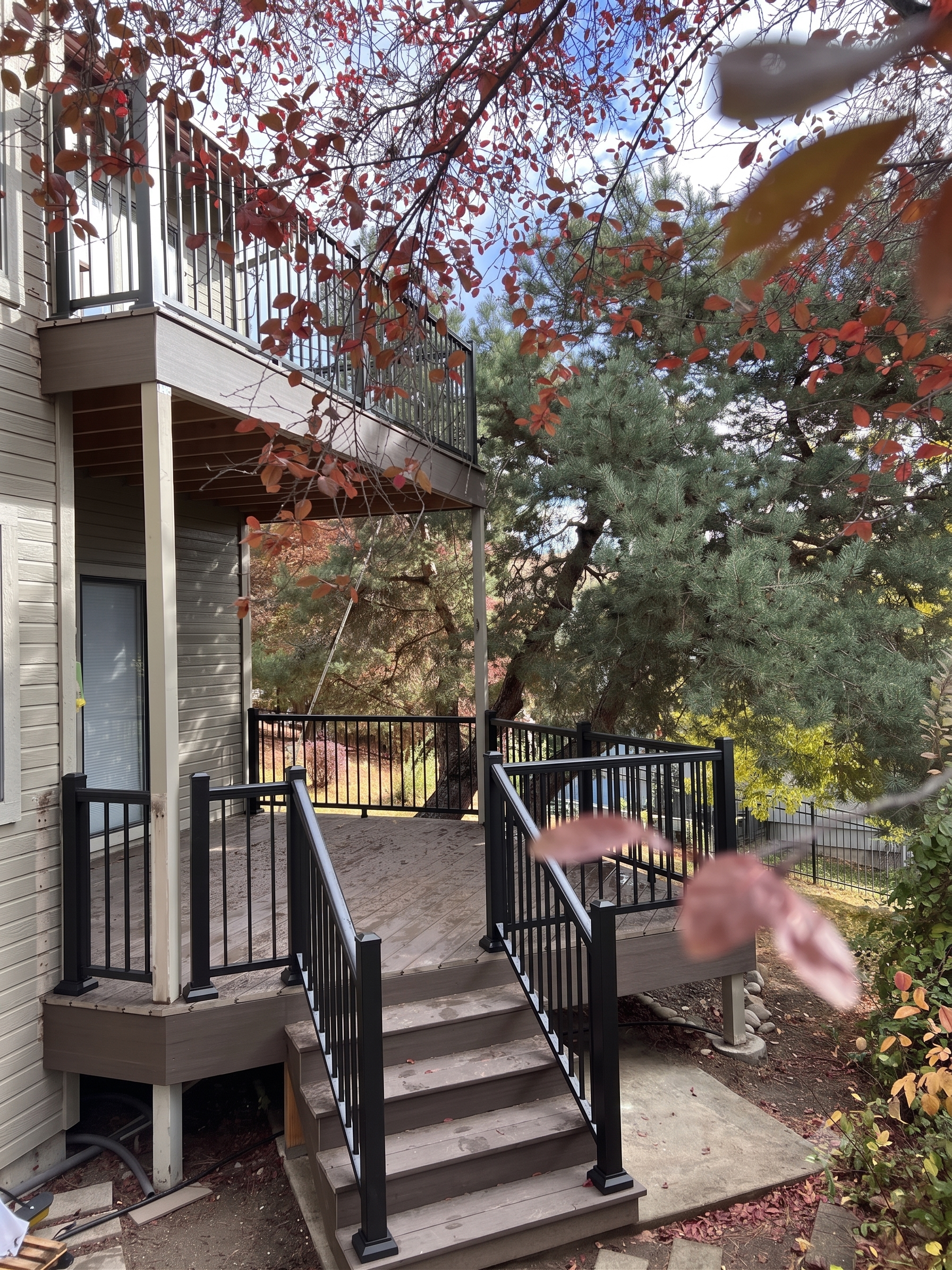 An elevated gray deck with black railings and stairs leading down to a grassy backyard.