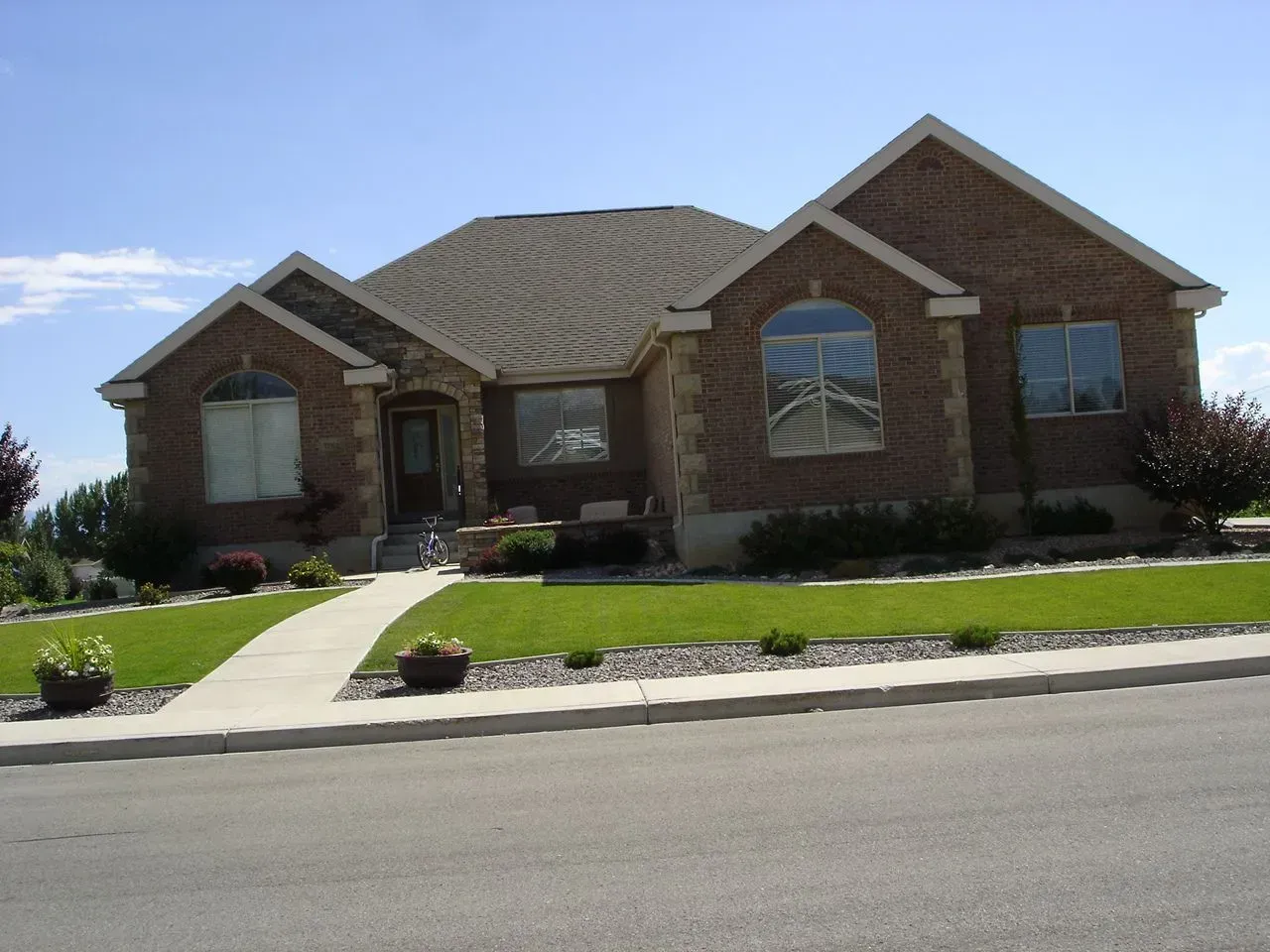 Brick suburban house with a front walkway, green lawn, and driveway under a blue sky