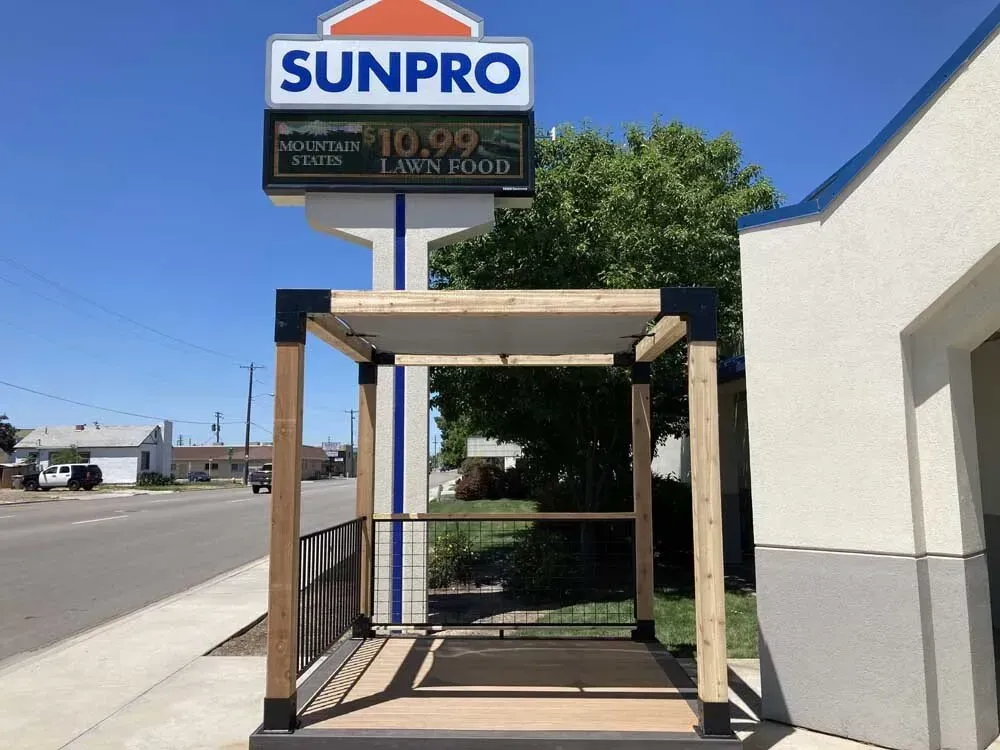 Simple wooden structure beside a SUNPRO storefront sign on a sunny sidewalk.