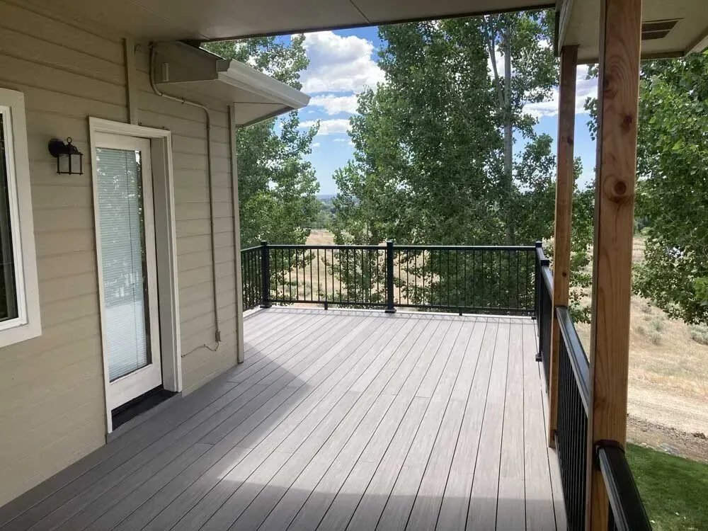 Covered wooden deck with railing and a view of trees and sky