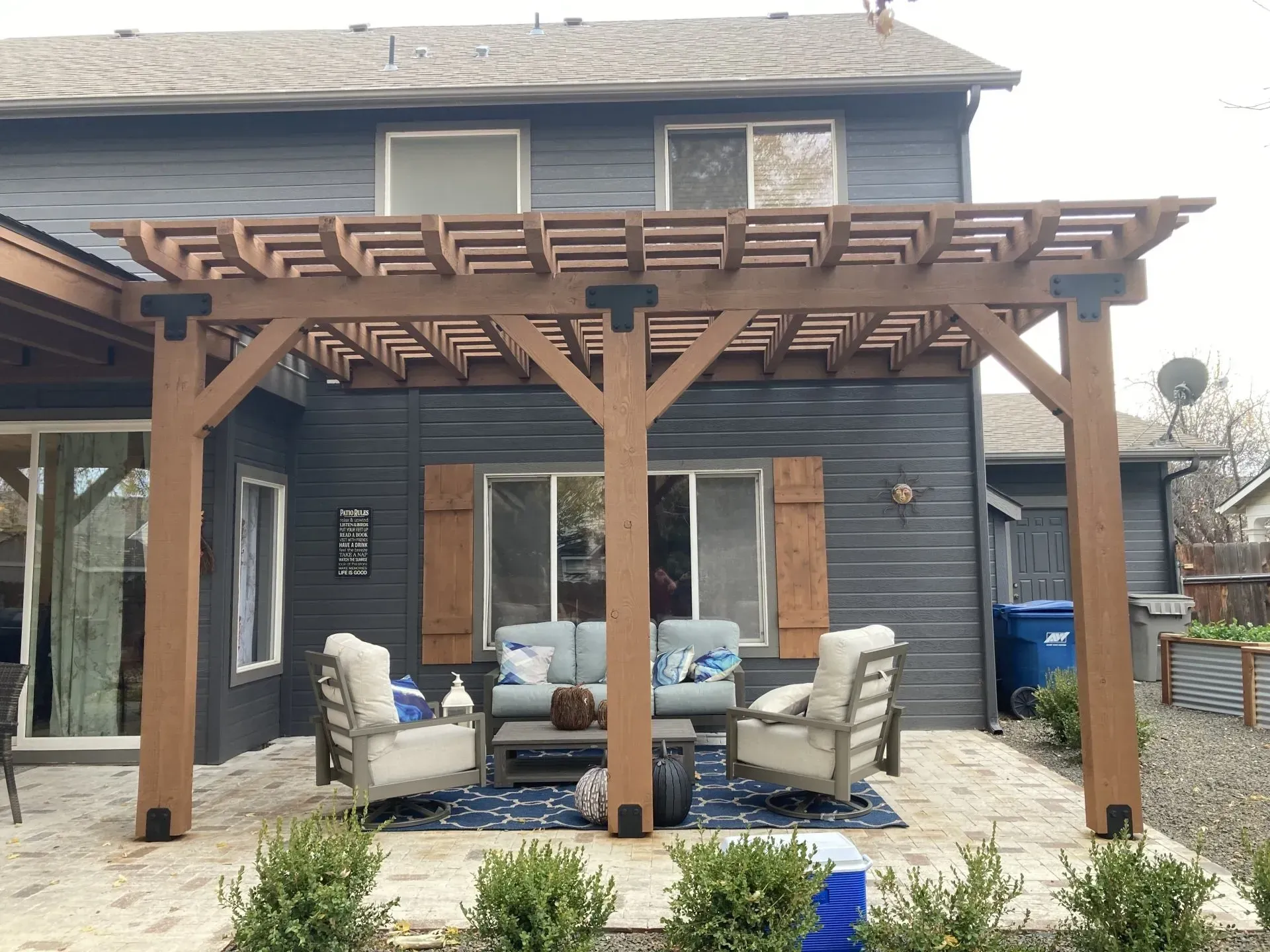 Backyard patio with wooden pergola, outdoor sectional seating, and stone pavers against a gray house