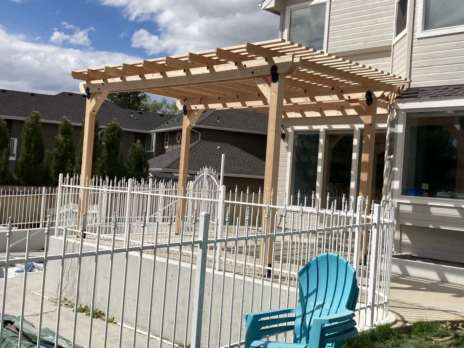 Wooden pergola and fenced patio with a blue chair in a sunlit courtyard