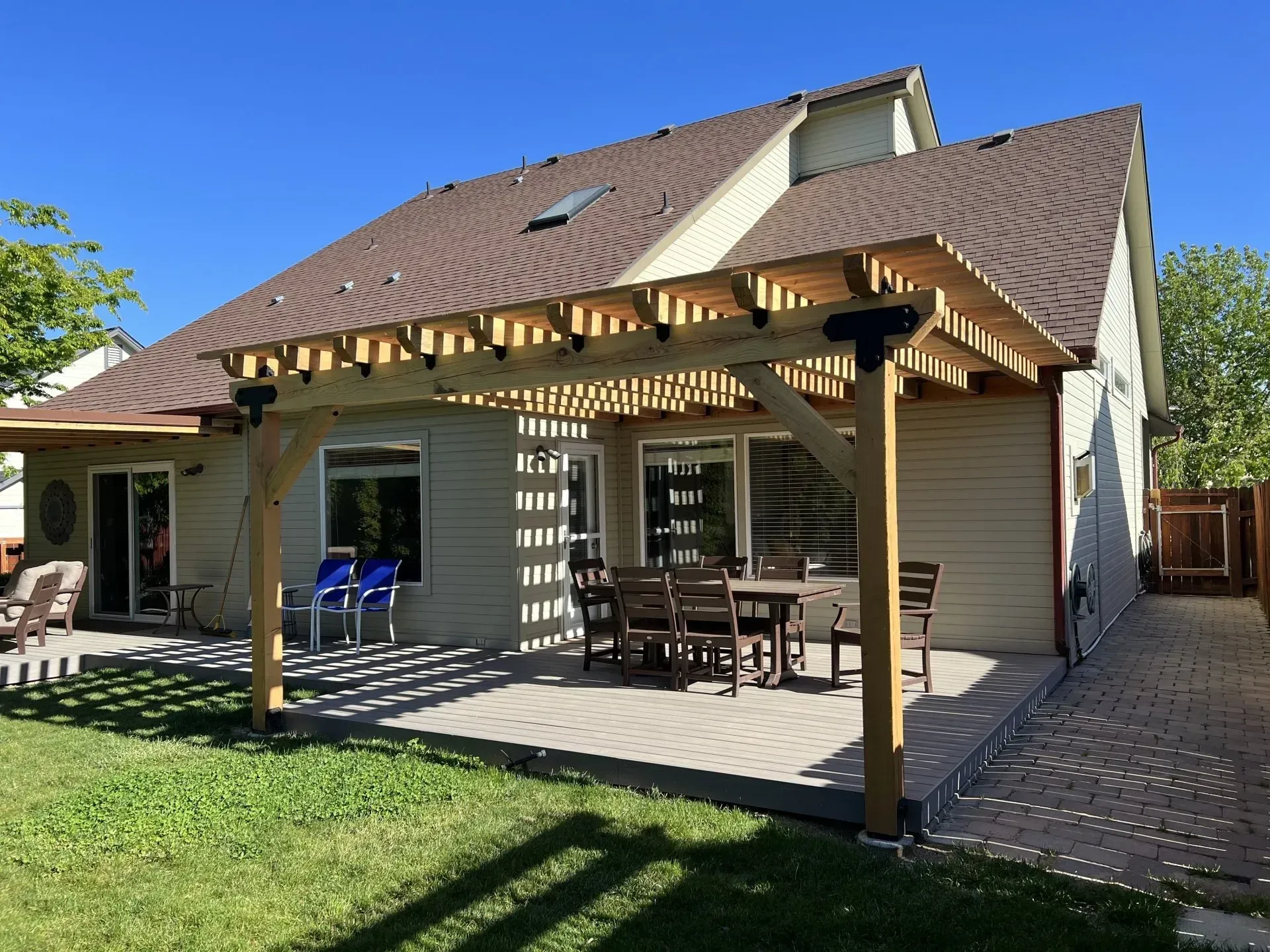 Covered patio with wooden pergola, dining table, and chairs beside a house and grassy backyard