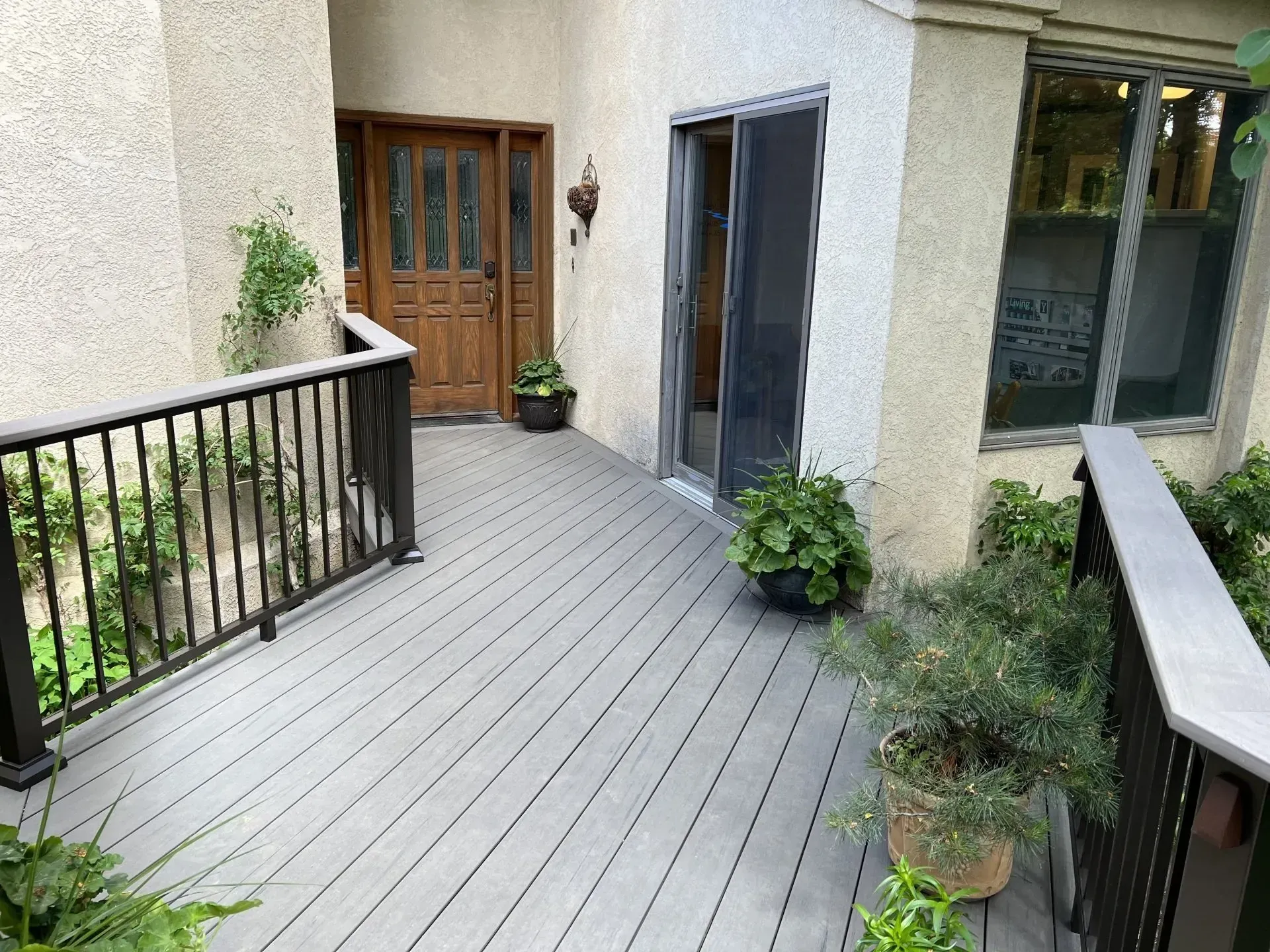 Wooden deck walkway with black railings leading to a front door and sliding glass door