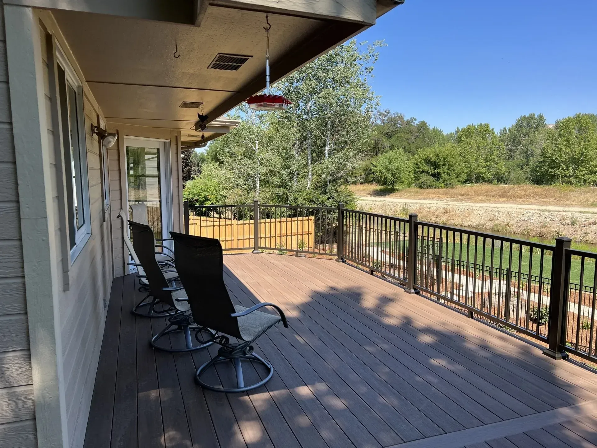 Covered wooden deck with black chairs, railing, and a view of trees and open fields