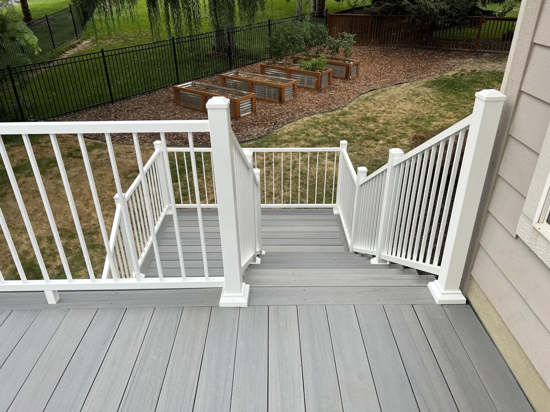 White backyard deck stairs descending to a fenced garden with mulch and greenery