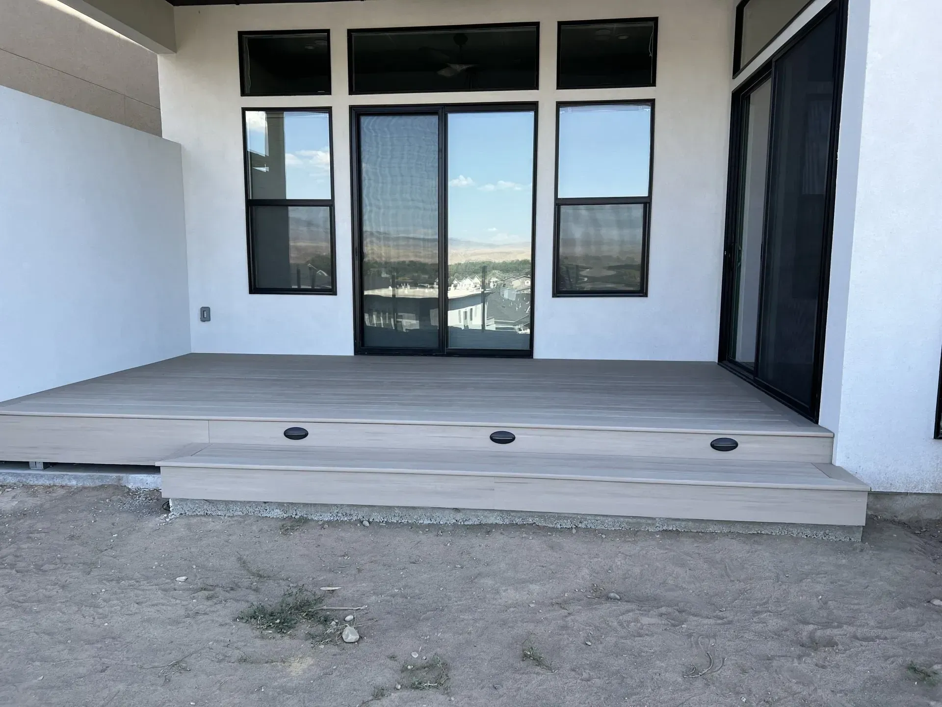 Front porch with white walls, black-framed windows, and a light gray deck above a gravel yard.