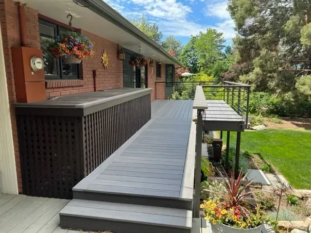 Long gray deck ramp beside a brick house, with railing and garden view.