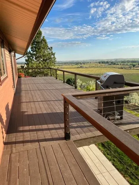Wooden deck with railing overlooking open fields under a blue sky