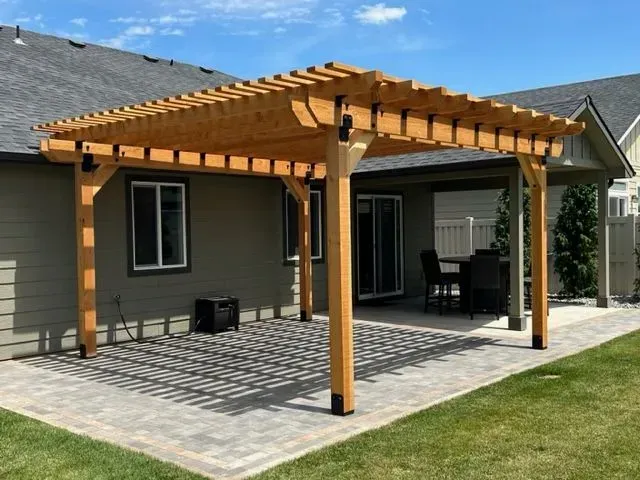 Wooden pergola patio over a concrete deck beside a house, with outdoor seating in a sunny yard