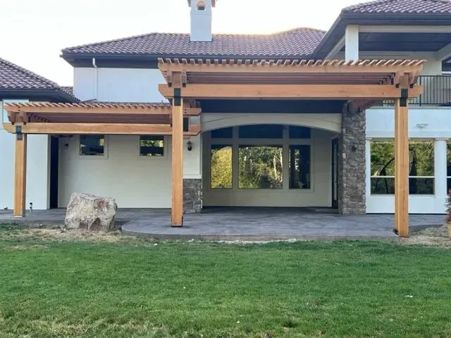 Modern house exterior with wooden pergola patio, large windows, and a grassy backyard.