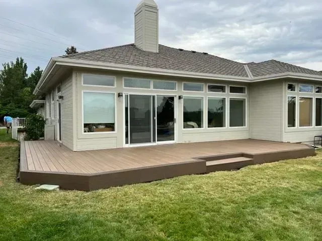 Modern house with large windows and a wooden deck beside a grassy yard