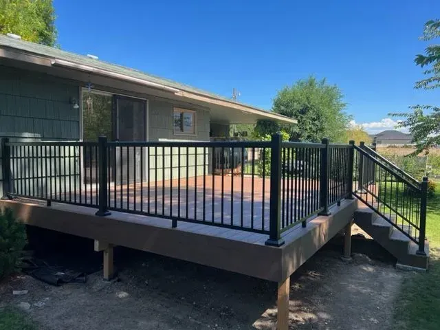 Raised wooden deck with black railing and stairs beside a house under a clear blue sky