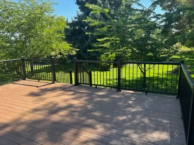 Wooden deck with black railings overlooking a green backyard and trees in bright sunlight